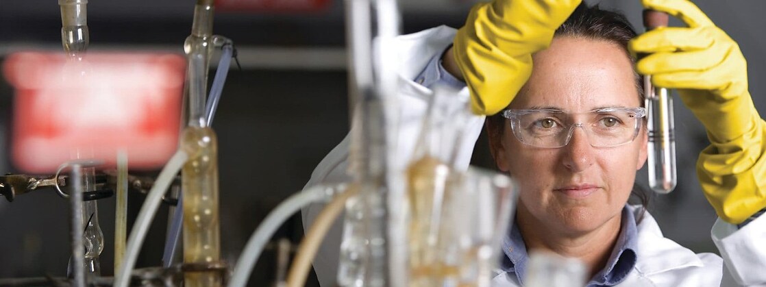 Scientist wearing protective wear and mixing with test tubes.