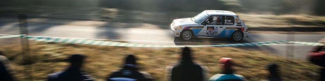 Rally car driving along a road in front of a crowd of spectators