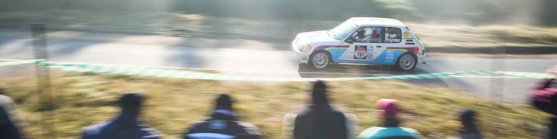 Rally car driving along a road in front of a crowd of spectators