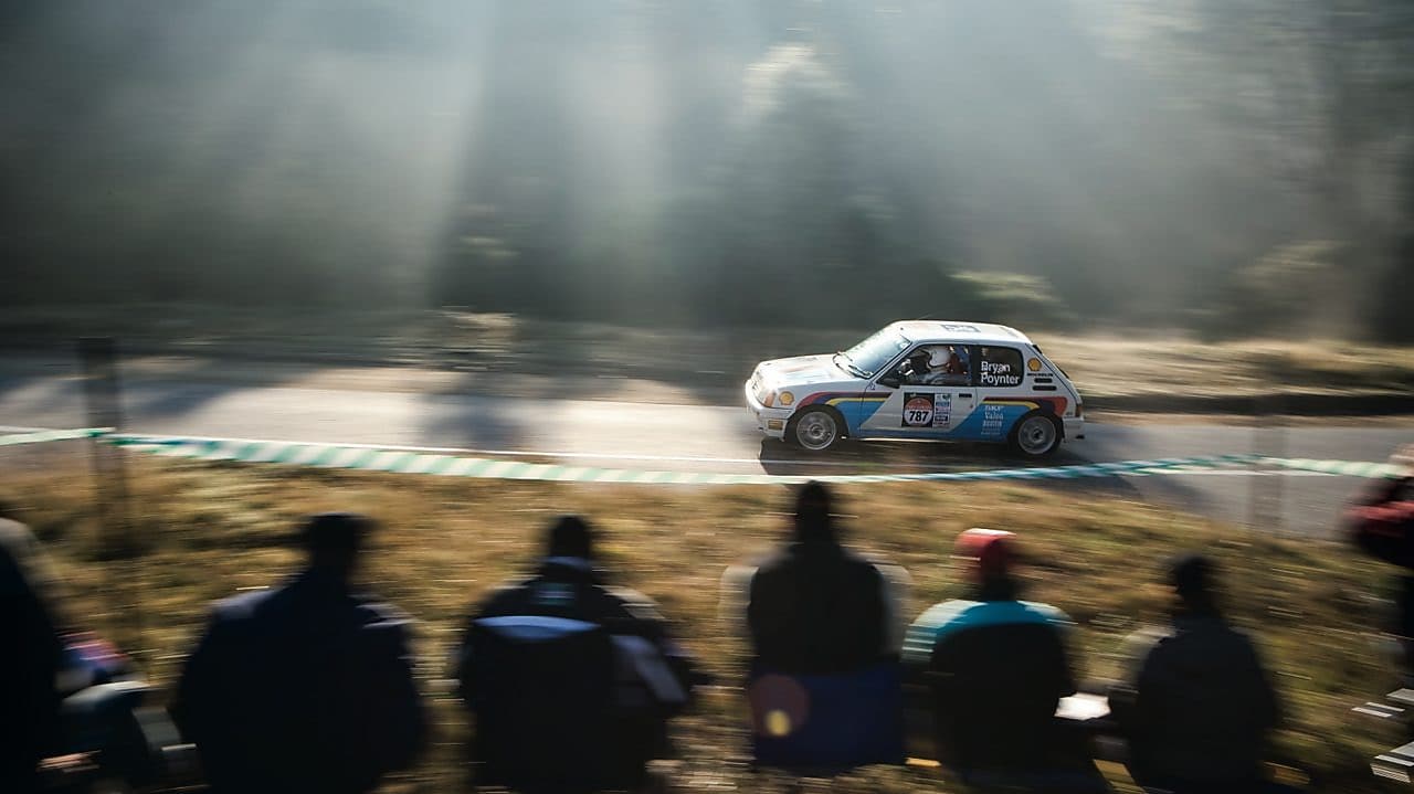 Rally car driving along a road in front of a crowd of spectators