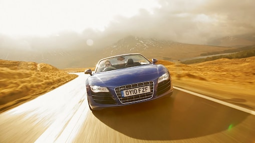  Open top blue car, face on view, driving through the countryside surrounded by mountain scenary