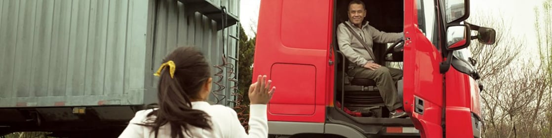 Man in red truck cab with door open waving to his daughter