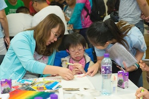 Devoted volunteer and teacher assisted student with special educational needs drawing and making decoration on recycling bag.