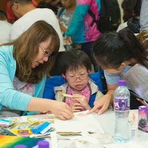 Devoted volunteer and teacher assisted student with special educational needs drawing and making decoration on recycling bag.
