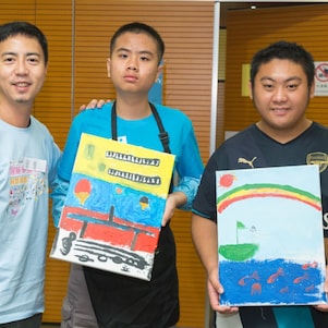 Students with special educational needs and volunteer took photo with paintings.