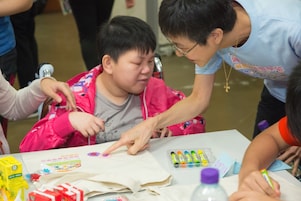 Devoted volunteer assisted student with special educational needs in drawing and making decoration on recycling bag.