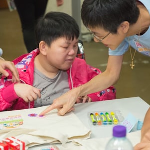 Devoted volunteer assisted student with special educational needs in drawing and making decoration on recycling bag.