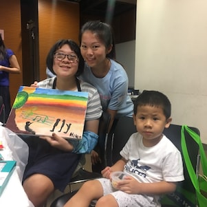 Student with special educational needs held her painting and took photo with parent and volunteer.